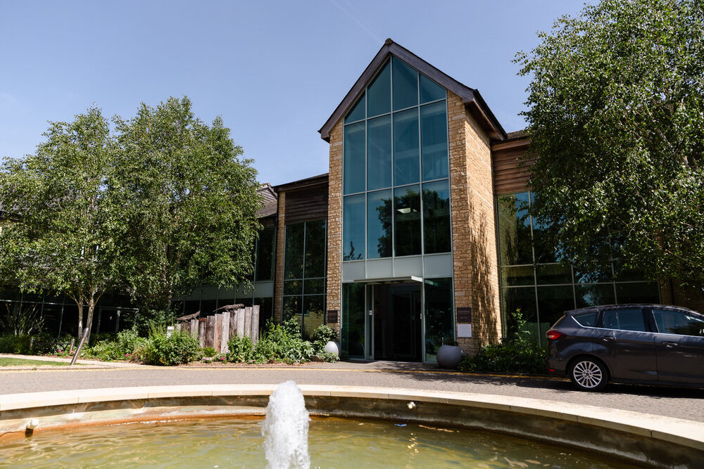 De Vere Cotswold Water Park Hotel main entrance with full-height glass frontage and courtyard fountain