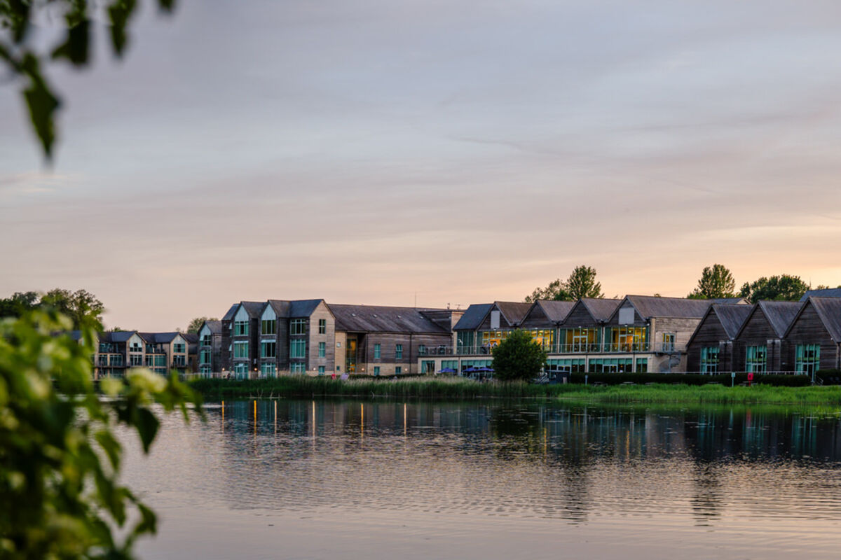 De Vere Cotswold Water Park hotel viewed across the lake at sunset — Gloucestershire wedding venue