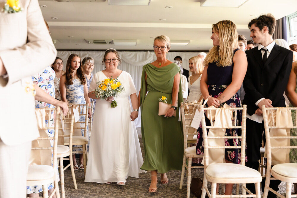 Bride walking down the aisle during an indoor wedding ceremony at De Vere Cotswold Water Park