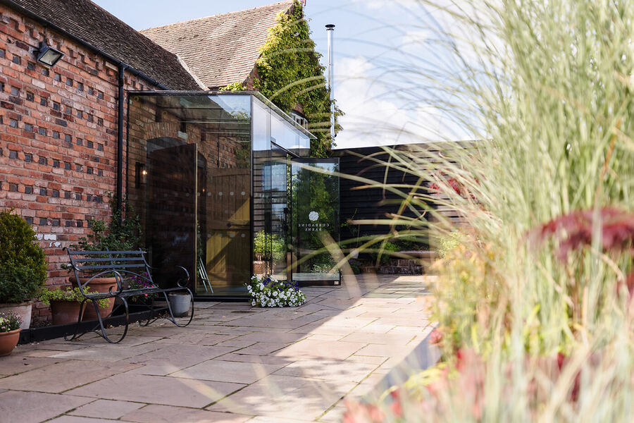 Curradine Barns courtyard with the glass entrance, stone patio and ornamental grasses on a summer wedding day