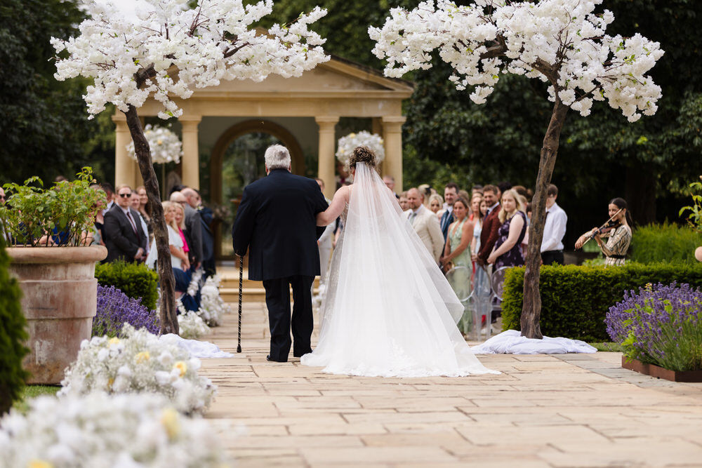 Bride walking down the aisle with her father at a Rowton Castle outdoor ceremony — Linden Belvedere in background