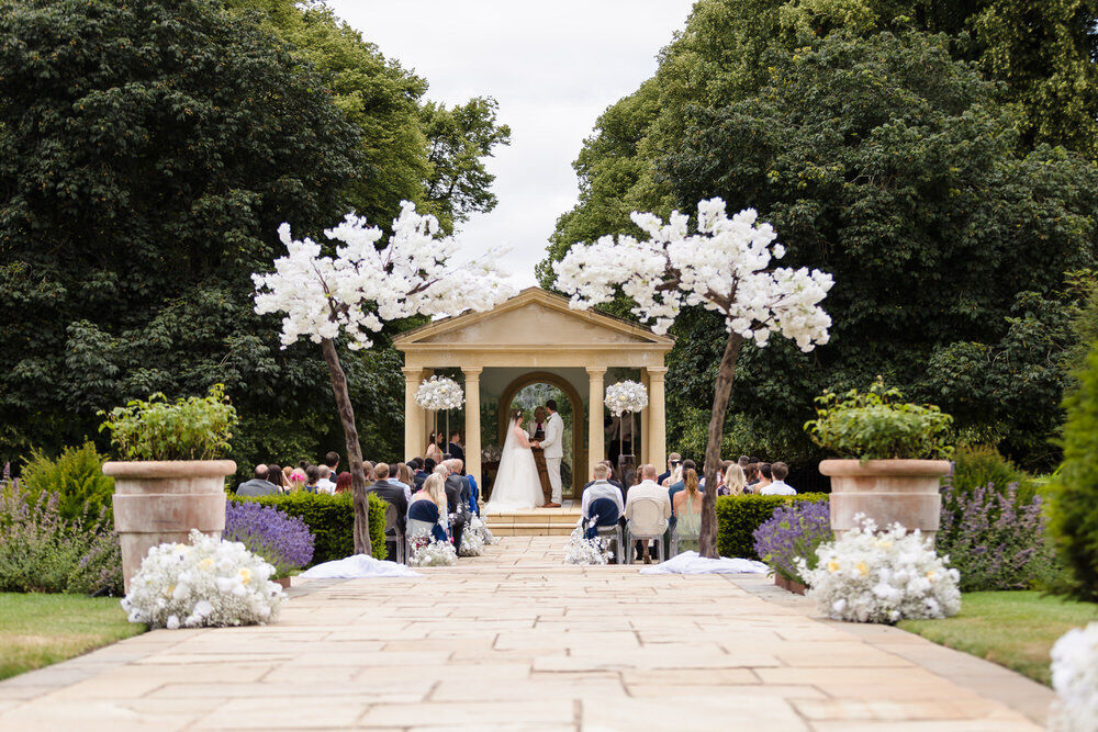 Wedding ceremony at the Linden Belvedere, Rowton Castle, Shropshire — couple exchanging vows outdoors with guests seated