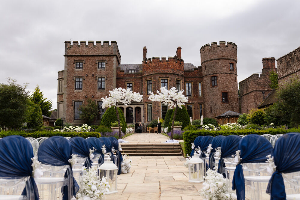 Outdoor wedding ceremony setup at Rowton Castle, Shropshire — white chairs with navy sashes facing the castle facade