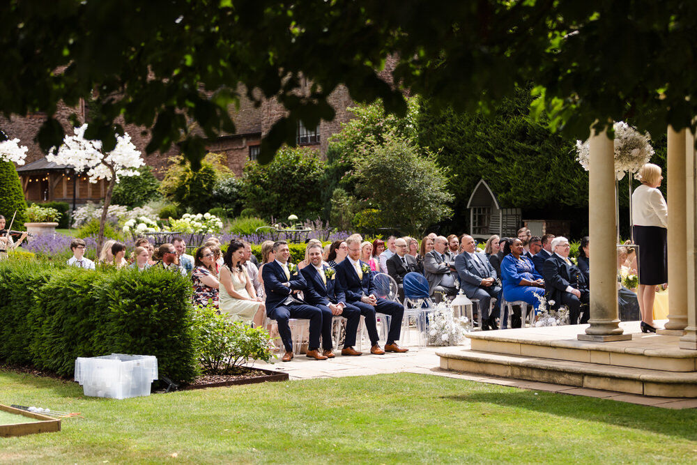 Wedding guests seated at a Rowton Castle outdoor ceremony — candid view through the gardens with the Linden Belvedere
